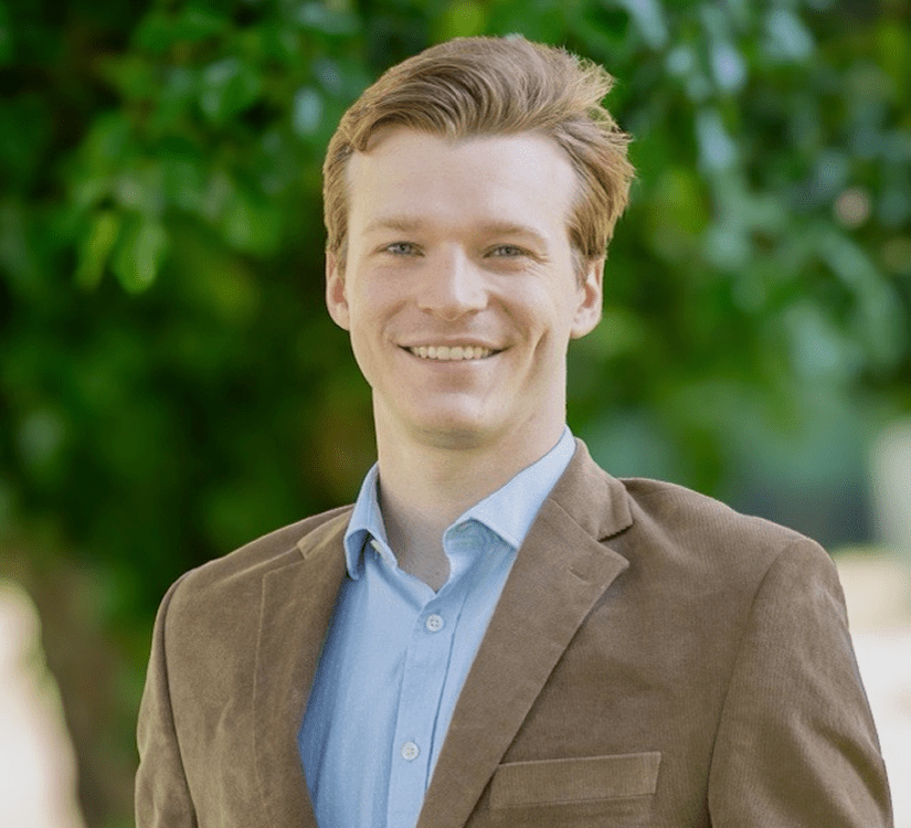 Smiling person in brown jacket, green background.
